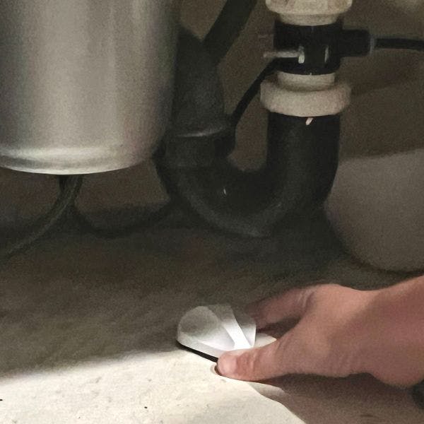 Woman placing Frontpoint water flood sensor under kitchen sink